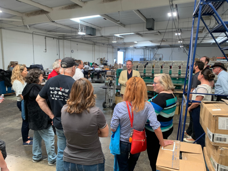 A group of people listening to Rob Watson speak on the Santa Ana production floor.