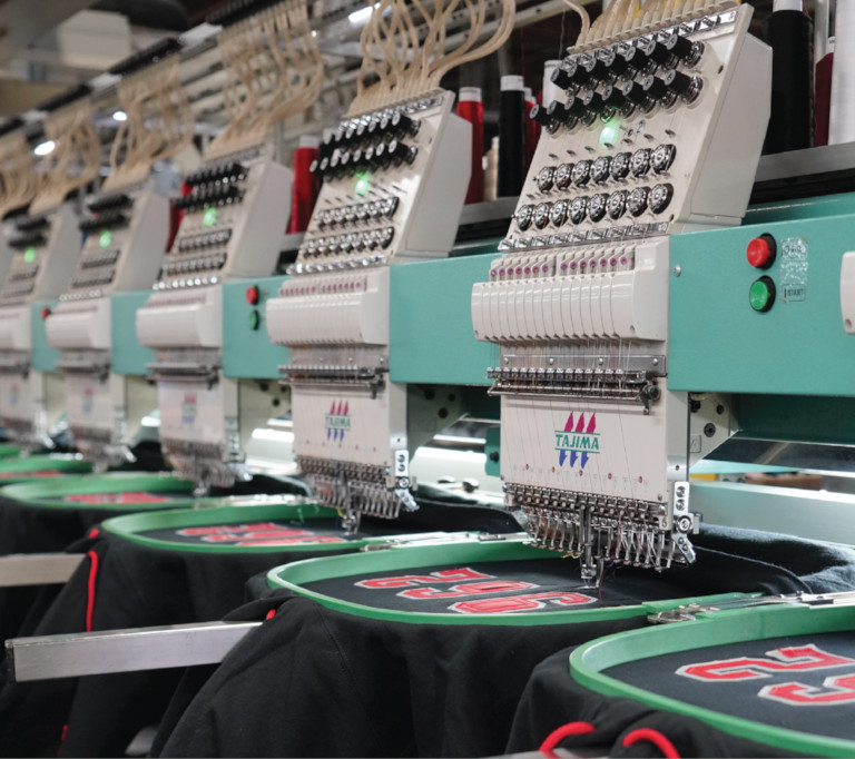 A row of embroidery machines embroidering black hoodies.