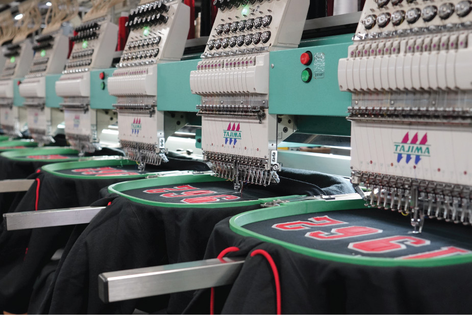 A row of embroidery machines embroidering black hoodies.